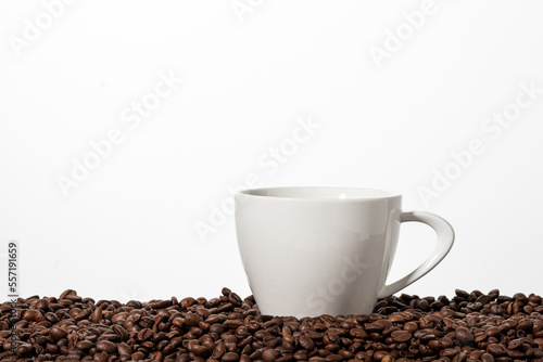 Filiżanka stojąca pomiędzy ziarnami kawy i białe tło.