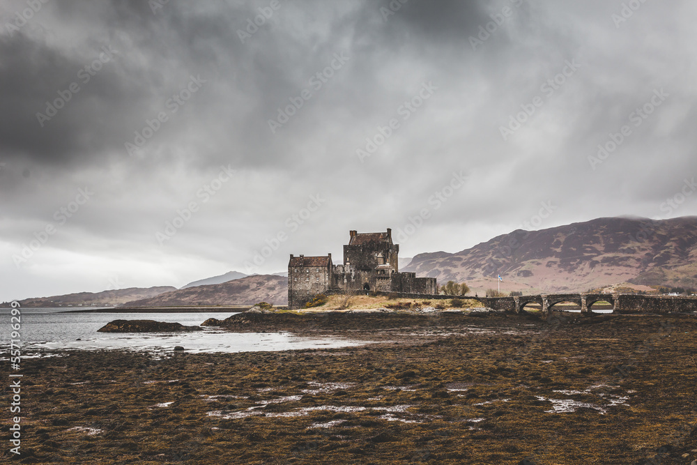 Eilean Donan Castle In Scotland. A old building standing on a small island surrounded by water. A bridge leading to the mainland. Mountain and hills surrounding the castle.