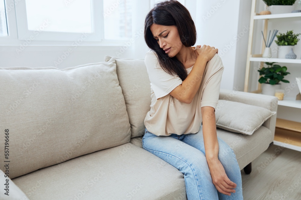 Woman sitting on sofa at home arm and shoulder pain, muscle sprain and joint pain, calcium problems in bones Woman sitting on sofa at home arm and shoulder pain, muscle sprain and joint pain, calcium problems in bones