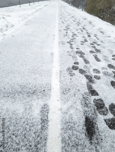 Snow-covered two-way road, footprints in the snow, heavy pedestrian traffic in winter.