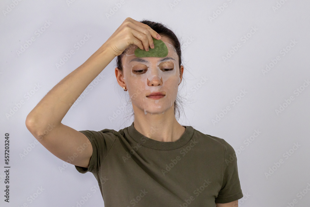Young woman performs a self-massage of her face with a Guasha scrub on a fabric mask with serum Young woman performs a self-massage of her face with a Guasha scrub on a fabric mask with serum