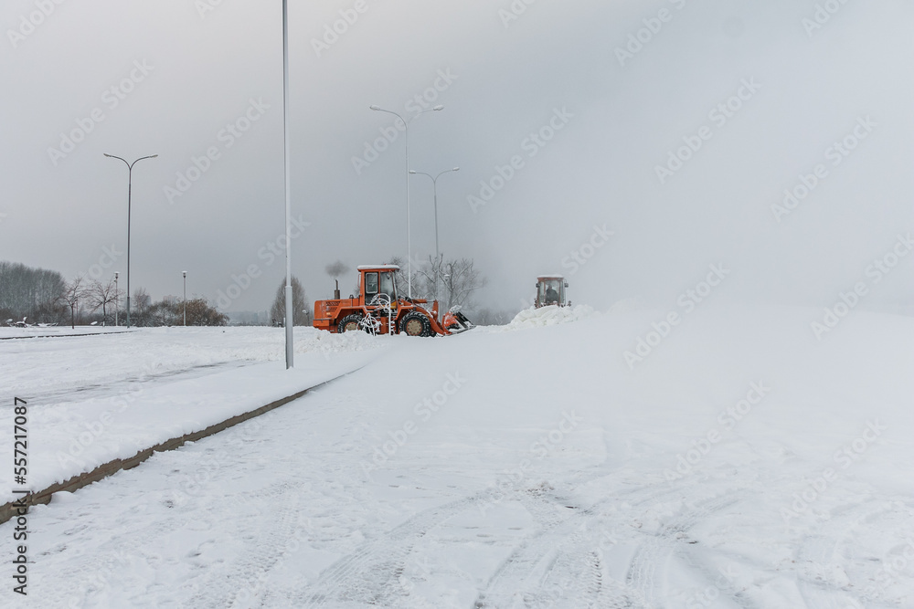 Bulldozers remove snow with an iron bucket after a blizzard. Cleaning snowdrifts with a bulldozer. Cleaning the city after a blizzard.