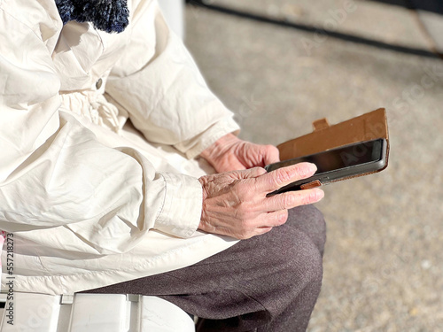 ベンチに座ってスマホを操作する高齢女性の手のアップ