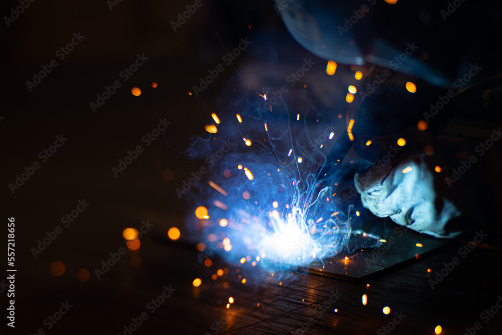 Metal welder works with a steel welder in a factory with protective equipment. Manufacture of metal structures and repair and construction services according to the concept of manual labor. Metal welder works with a steel welder in a factory with protective equipment. Manufacture of metal structures and repair and construction services according to the concept of manual labor.