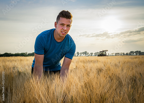 Junger sportlicher Landwirt steht gebeugt in einem Getreidefeld bei stimmungsvollen Licht.