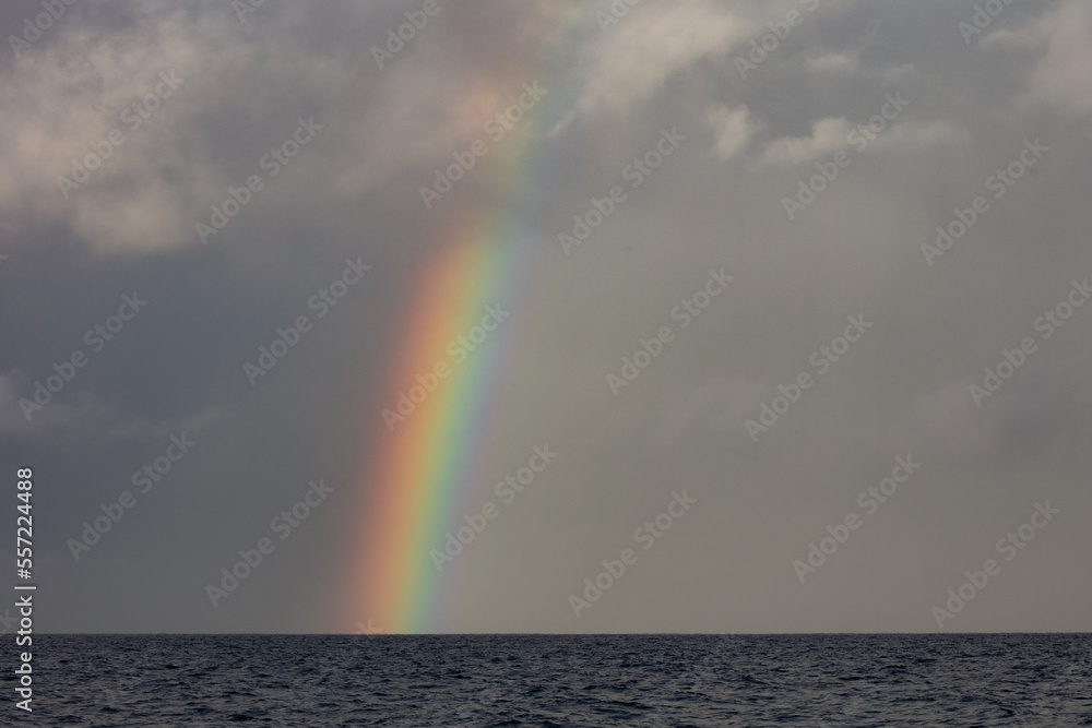 A bright rainbow appears over the South Pacific Ocean during the monsoon season.