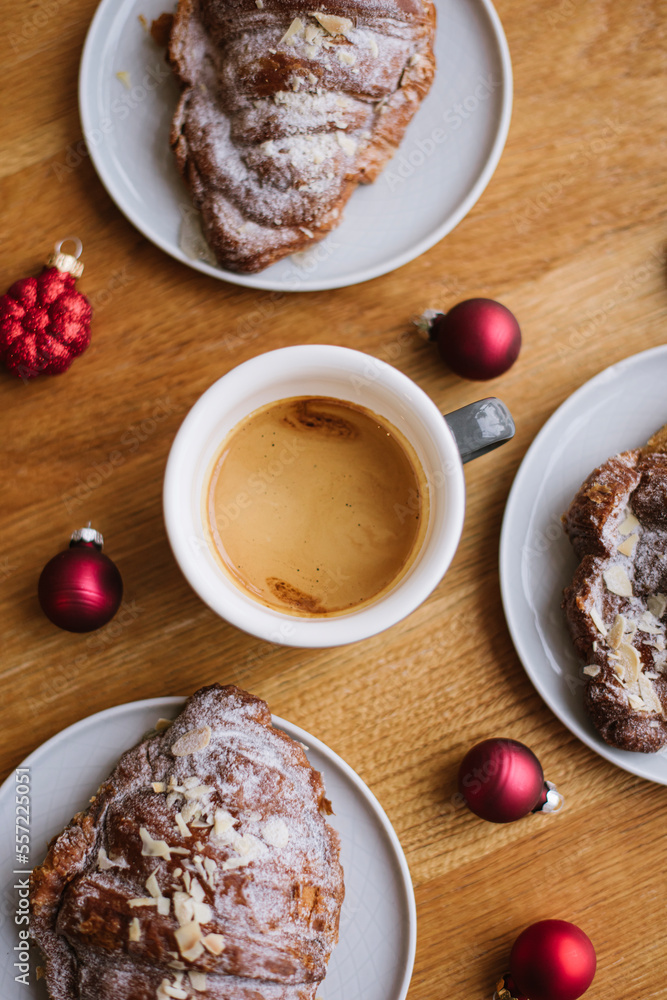Delicious freshly brewed espresso coffee with a beautiful thick crema, standing on the wooden table with almond croissants, decorated with small red ornament Christmas balls, close up vertical image Delicious freshly brewed espresso coffee with a beautiful thick crema, standing on the wooden table with almond croissants, decorated with small red ornament Christmas balls, close up vertical image