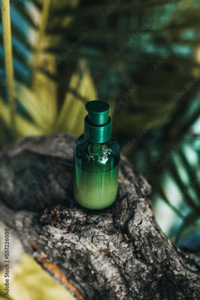 Green bottle of face serum on a wooden stand against tropical palms. Skin care natural cosmetics Green bottle of face serum on a wooden stand against tropical palms. Skin care natural cosmetics