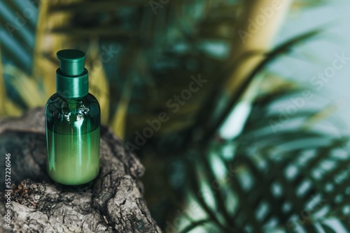 Green bottle of face serum on a wooden stand against tropical palms. Natural skin care cosmetics © asauriet