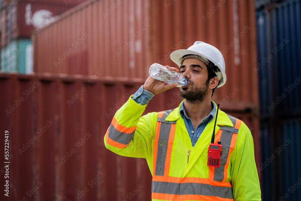 Workers or engineers drink water to quench their thirst at the container yard. Working on hot days. The concept of transportation in a container warehouse. Workers or engineers drink water to quench their thirst at the container yard. Working on hot days. The concept of transportation in a container warehouse.