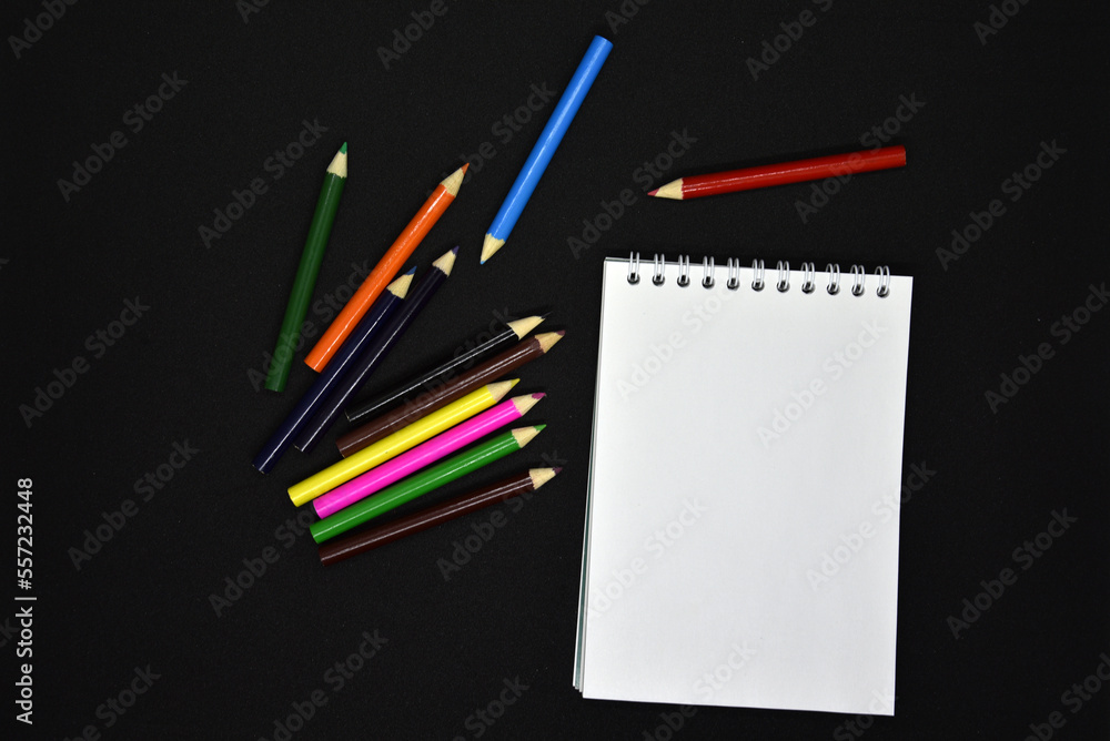 Colored pencils on a black background. Notepad and pencils. Colored pencils on a black background. Notepad and pencils.