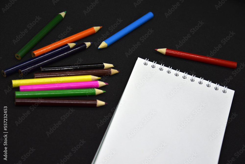 Colored pencils on a black background. Notepad and pencils. Colored pencils on a black background. Notepad and pencils.