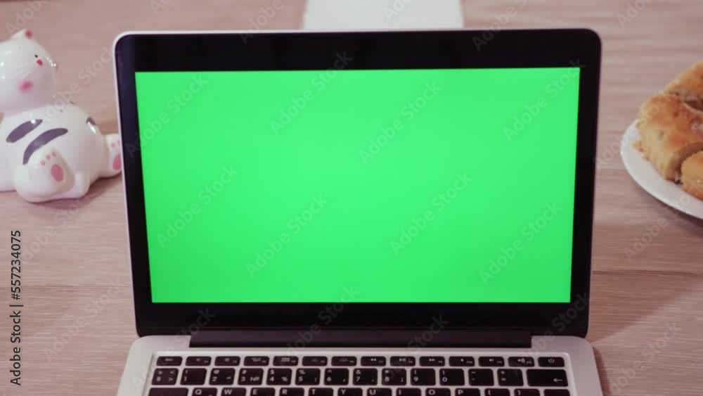 Green chromakey screen of modern laptop standing on wooden table near plate with bakery. Open gadget ready for use in kitchen closeup Green chromakey screen of modern laptop standing on wooden table near plate with bakery. Open gadget ready for use in kitchen closeup