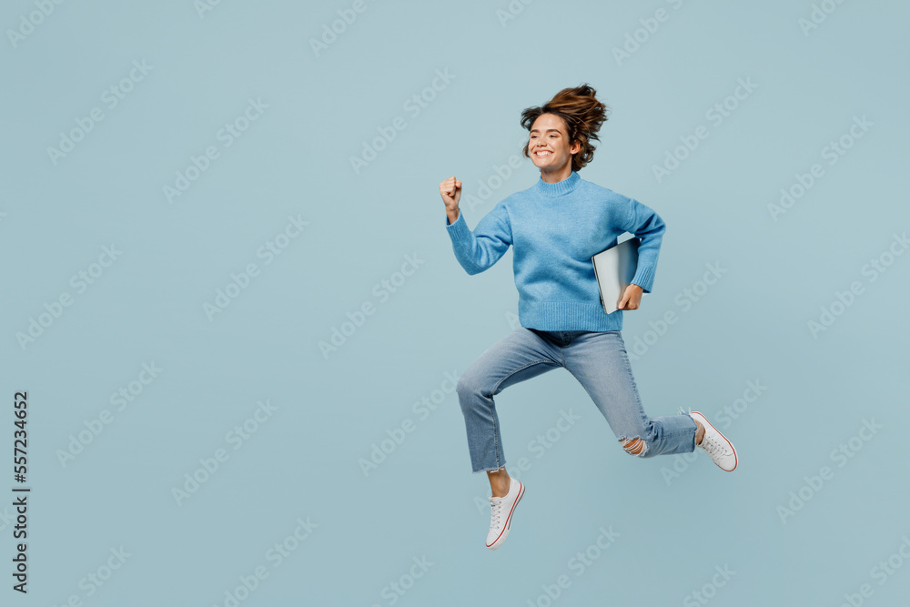 Full body side view fun surprised smart young IT woman wear knitted sweater hold closed laptop pc computer run fast isolated on plain pastel light blue cyan background studio People lifestyle concept.