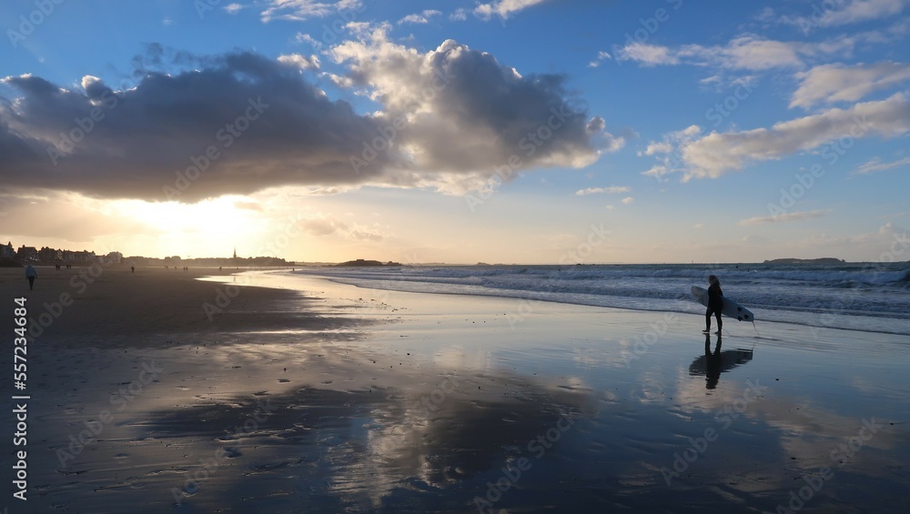 Surfeuse marchant sur le sable, au bord de la mer, avec sa planche de surf sous le bras, sur la plage du Sillon à Saint-Malo, en Bretagne (France) Surfeuse marchant sur le sable, au bord de la mer, avec sa planche de surf sous le bras, sur la plage du Sillon à Saint-Malo, en Bretagne (France)