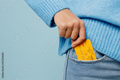 Cuadro en lienzo Close up cropped woman wearing knitted sweater hold in hand put into pocket mock up of credit bank card isolated on plain pastel light blue cyan background studio portrait