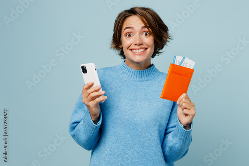 Traveler woman wears sweater hold passport ticket use mobile phone isolated on plain light blue cyan background Tourist travel abroad in free spare time rest getaway Air flight trip journey concept. #557234672