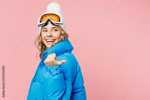 Snowboarder fun woman wear blue suit goggles mask hat ski padded jacket point thumb finger back on area isolated on plain pastel pink background. Winter extreme sport hobby weekend trip relax concept.
