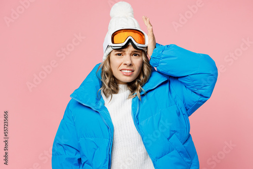 Snowboarder disappointed worried sad woman wear blue suit goggles mask hat ski padded jacket hold head isolated on plain pastel pink background. Winter extreme sport hobby weekend trip relax concept.