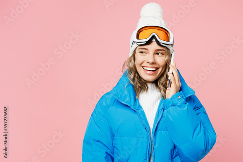 Snowboarder fun woman wear blue suit goggles mask hat ski padded jacket talk speak on mobile cell phone isolated on plain pastel pink background. Winter extreme sport hobby weekend trip relax concept.