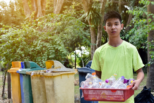 Portrait young asian boy holds plastic basket which has bottles from seperating bins behind him, environment care concept, soft and selective focus. photo