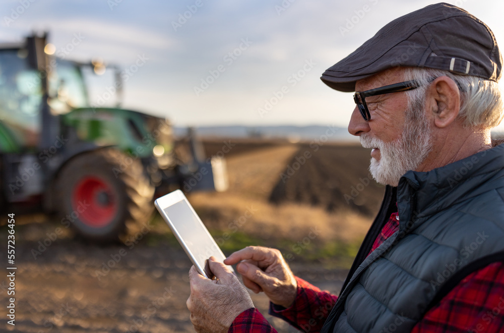 Senior farmer with tablet in field with tractor in background
