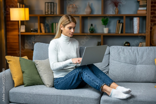 Portrait of a adult female freelancer sitting on the couch and working on project, watching movie on laptop, studying, blogging, resting and chatting online.