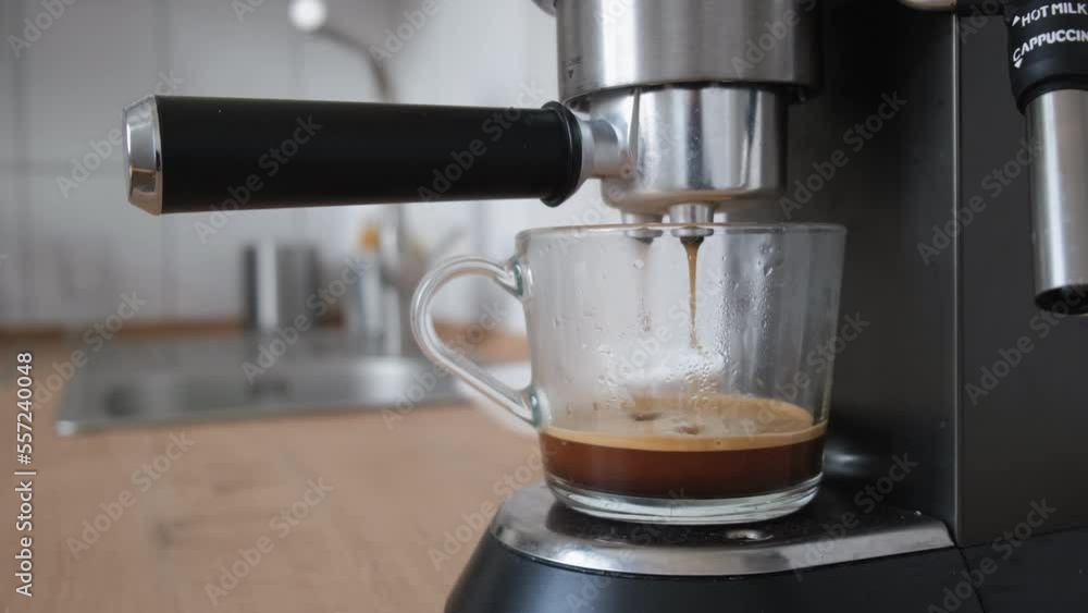 Process of making coffee by coffee machine into glass transparent cup, espresso coffee coming out from an automated coffemaker machine. inscription: cappuccino and hot milk Process of making coffee by coffee machine into glass transparent cup, espresso coffee coming out from an automated coffemaker machine. inscription: cappuccino and hot milk