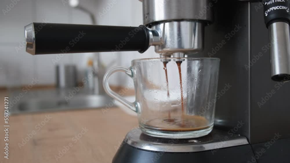 Process of making coffee by coffee machine into glass transparent cup, espresso coffee coming out from an automated coffemaker machine. inscription: cappuccino and hot milk Process of making coffee by coffee machine into glass transparent cup, espresso coffee coming out from an automated coffemaker machine. inscription: cappuccino and hot milk