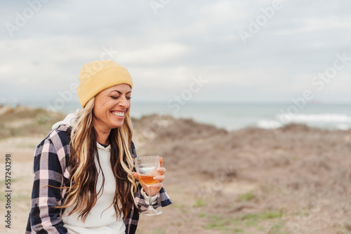 traveler nomad woman in winter laughing holding a glass with beer on coastal spot