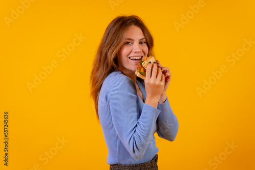 Woman eating a sandwich on a yellow background, healthy and vegetarian food