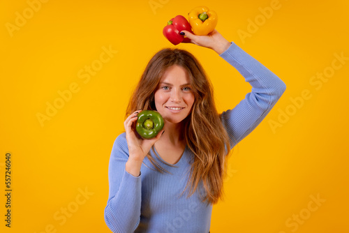 Vegetarian woman with green  yellow and red bell peppers on a yellow background  healthy food