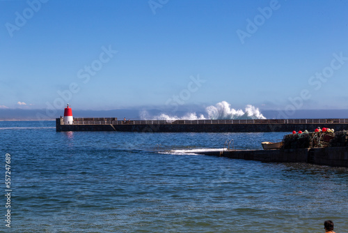 Muelle con un pequeño faro rojo y una ola rompiendo por encima. Corrubedo, A Coruña, España. photo