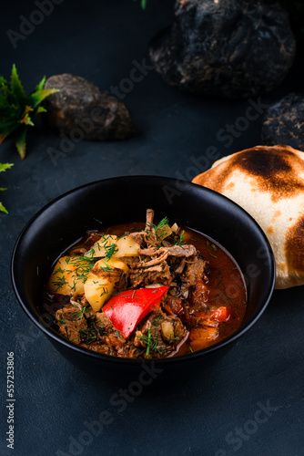 Stewed beef with potatoes, sweet peppers, onions in tomato sauce with herbs and flatbread on a dark table.