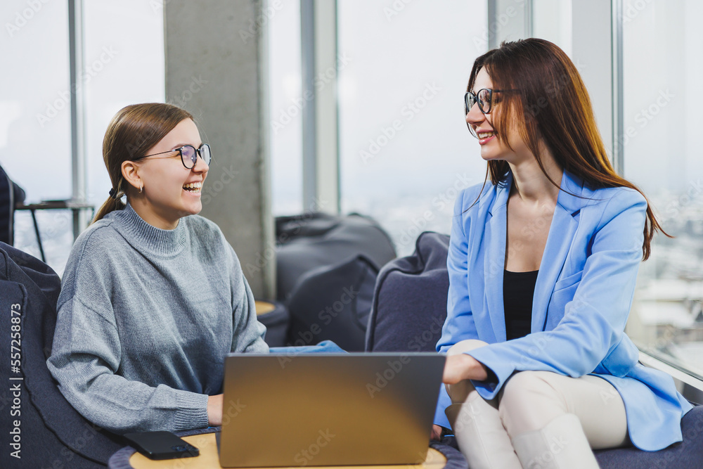 Two young female freelancers working remotely in the lounge area at a laptop. The concept of remote work Two young female freelancers working remotely in the lounge area at a laptop. The concept of remote work