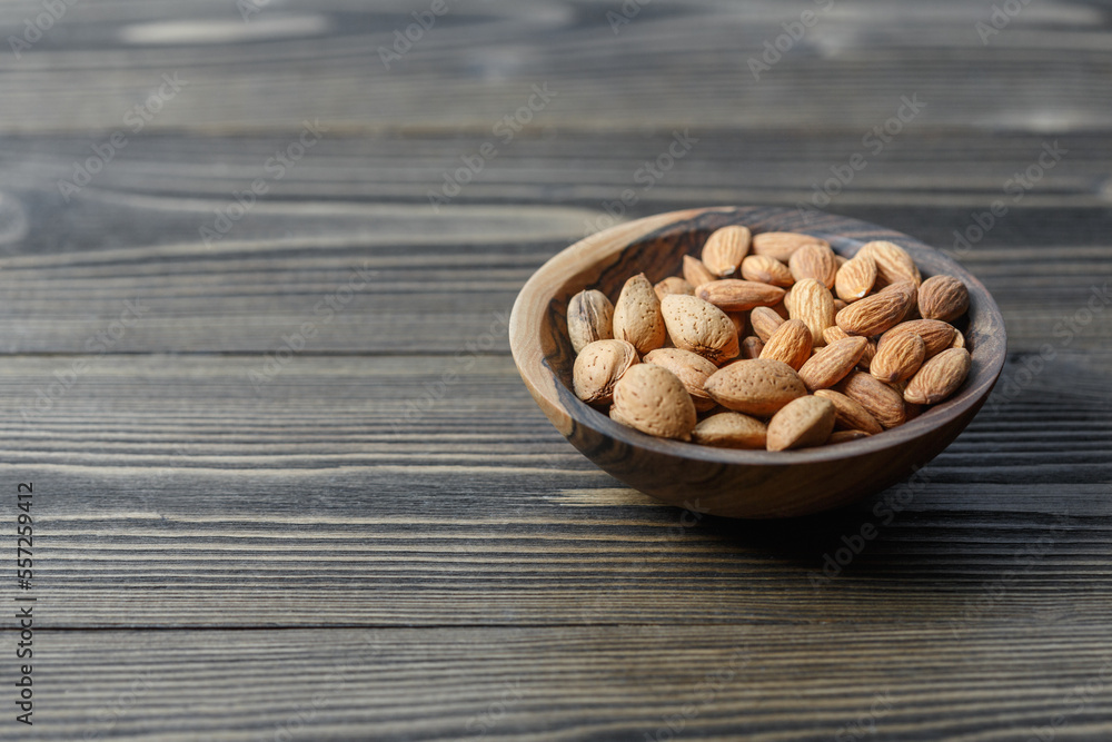 Peeled raw almonds and almonds in a shell in a wooden bowl on a dark wooden background. Peeled raw almonds and almonds in a shell in a wooden bowl on a dark wooden background.
