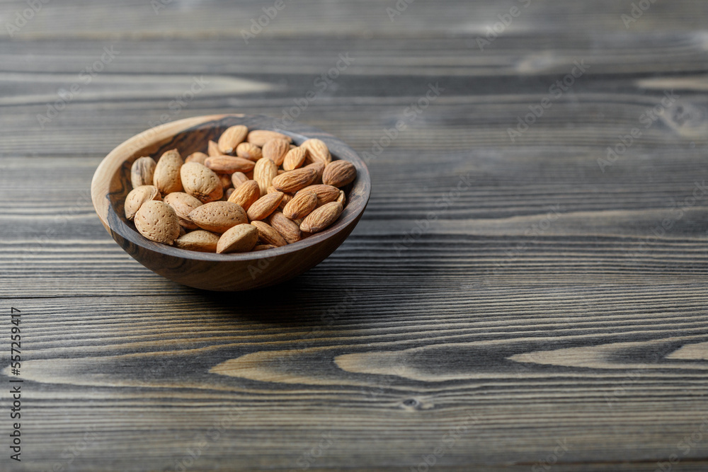 Peeled raw almonds and almonds in a shell in a wooden bowl on a dark wooden background.