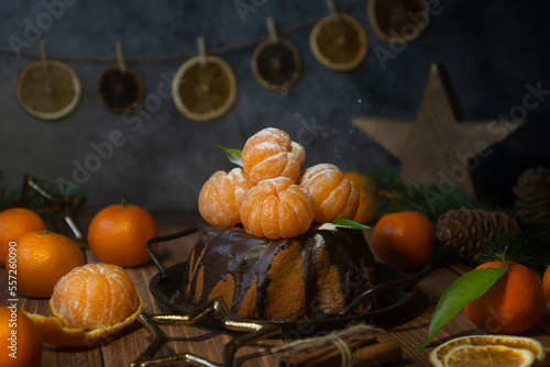 Homemade delicious christmas or new year cake with tangerines on a wooden background with coniferous branches.