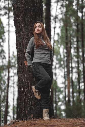 brown-haired caucasian girl next to a tree in the middle of the forest