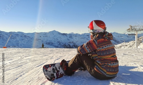 girl waits sitting in the snow at sunset with her snowboard in the french ski resort of val thorens photo