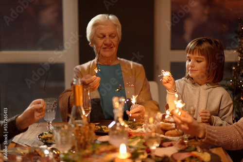 Horizontal portrait of senior woman and little girl burning sparklers at Xmas party photo