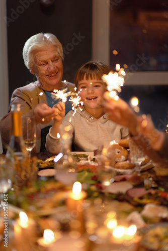 Vertical portrait shot of senior lady sitting with girl burning sparklers at Xmas party smiling