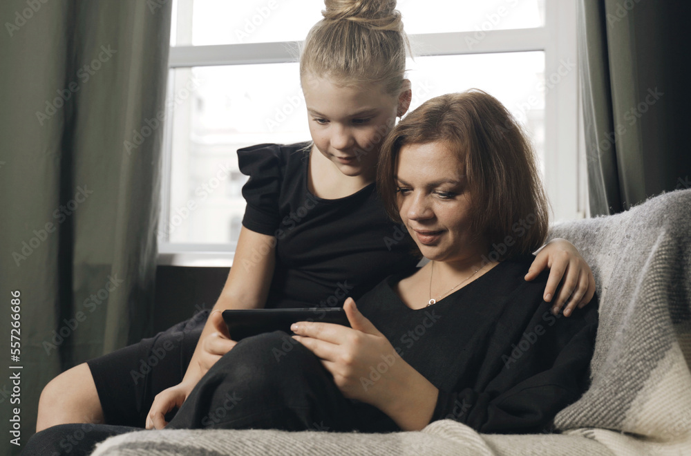 The daughter hugs her mother, they look at the tablet together, play, communicate. The daughter hugs her mother, they look at the tablet together, play, communicate.