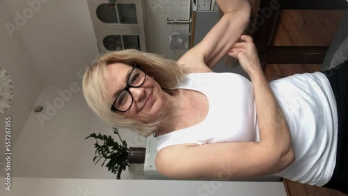 A woman with glasses touches her flabby hand and smiles. Vertical view