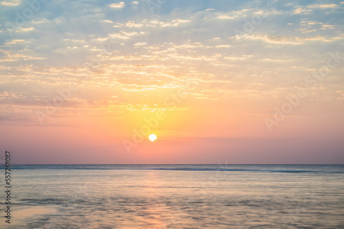 Beautiful sunrise at sea. Dawn on the Red Sea. The sun is reflected in the sea. Light clouds in the blue dawn sky. Tropical sunrise.Flattened sea in long exposure