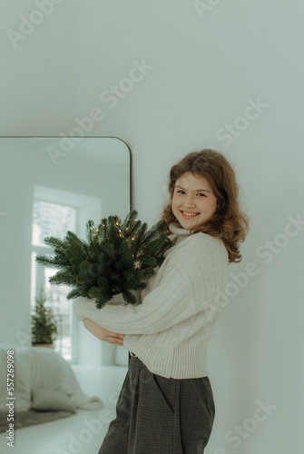 Beautiful festive portrait of a teen girl. Christmas light home background. Waiting for a miracle make a wish under the Christmas tree. Charming smile. New Year's holiday atmosphere