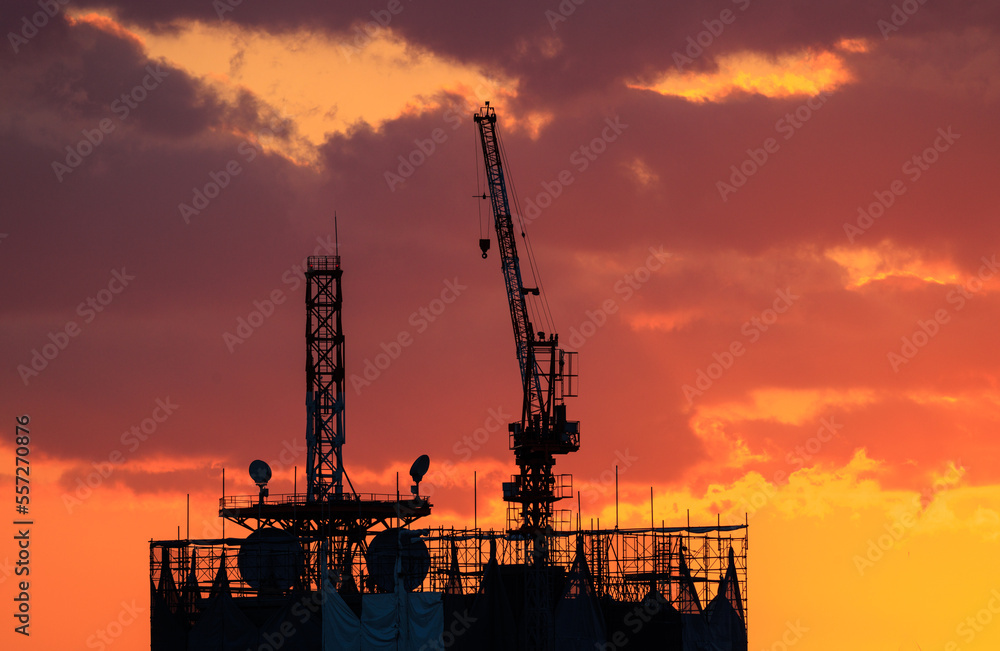 Construction crane atop unfinished building with beautiful sunset sky