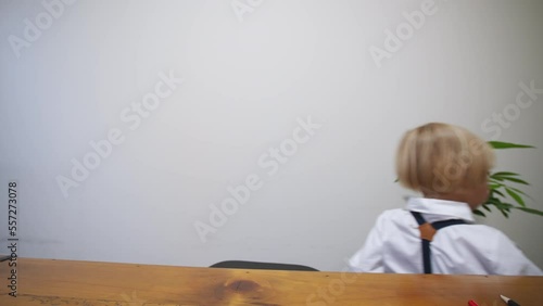 5 years old caucasian boy dressed smart in white shirt and black tie bow takes away a big black notebok with banknotes in it. Little accountant hides banknotes in the notebook photo