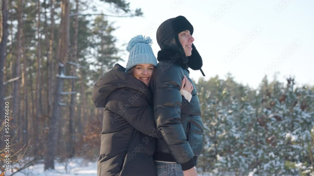 Side view smiling woman looking at camera hugging man standing in winter forest looking away. Loving excited Caucasian wife enjoying vacations with husband outdoors. Slow motion Side view smiling woman looking at camera hugging man standing in winter forest looking away. Loving excited Caucasian wife enjoying vacations with husband outdoors. Slow motion