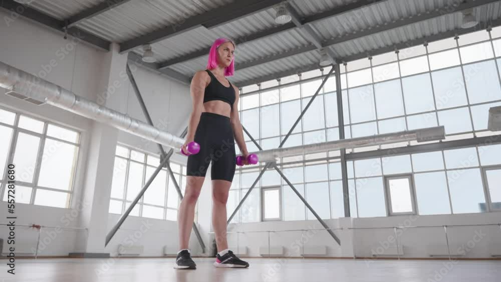 Young, caucasian woman with pink-colored hair doing dumbbell exercises. Low-angle view of fitness activity in a beautiful, bright studio. High quality 4k footage Young, caucasian woman with pink-colored hair doing dumbbell exercises. Low-angle view of fitness activity in a beautiful, bright studio. High quality 4k footage